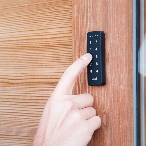 Jemand öffnet seine Haustür durch Zahlencodeeingabe am Keypad und daraufhin öffnet das Smartlock die Tür